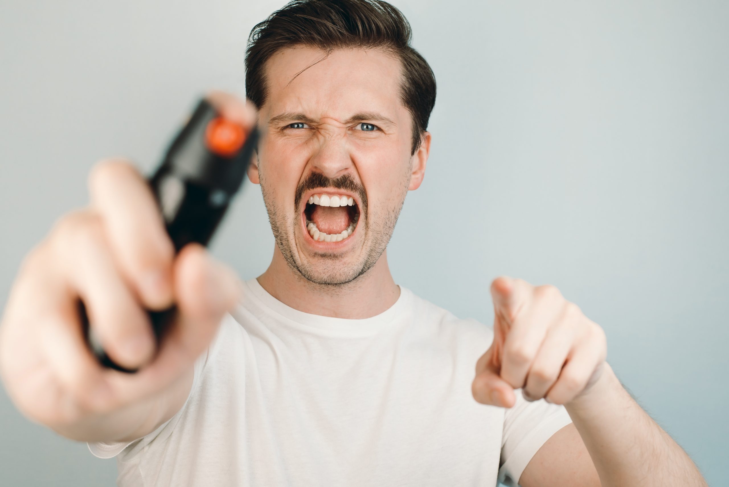 Man using self-defense device, close-up, selective focus. Young man holding pepper spray, screams and points his finger at the camera.